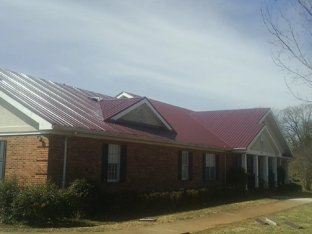 Red metal roof with gabled entries on a long brick building, from a Hail Damage Roof Repair job in Deckerville