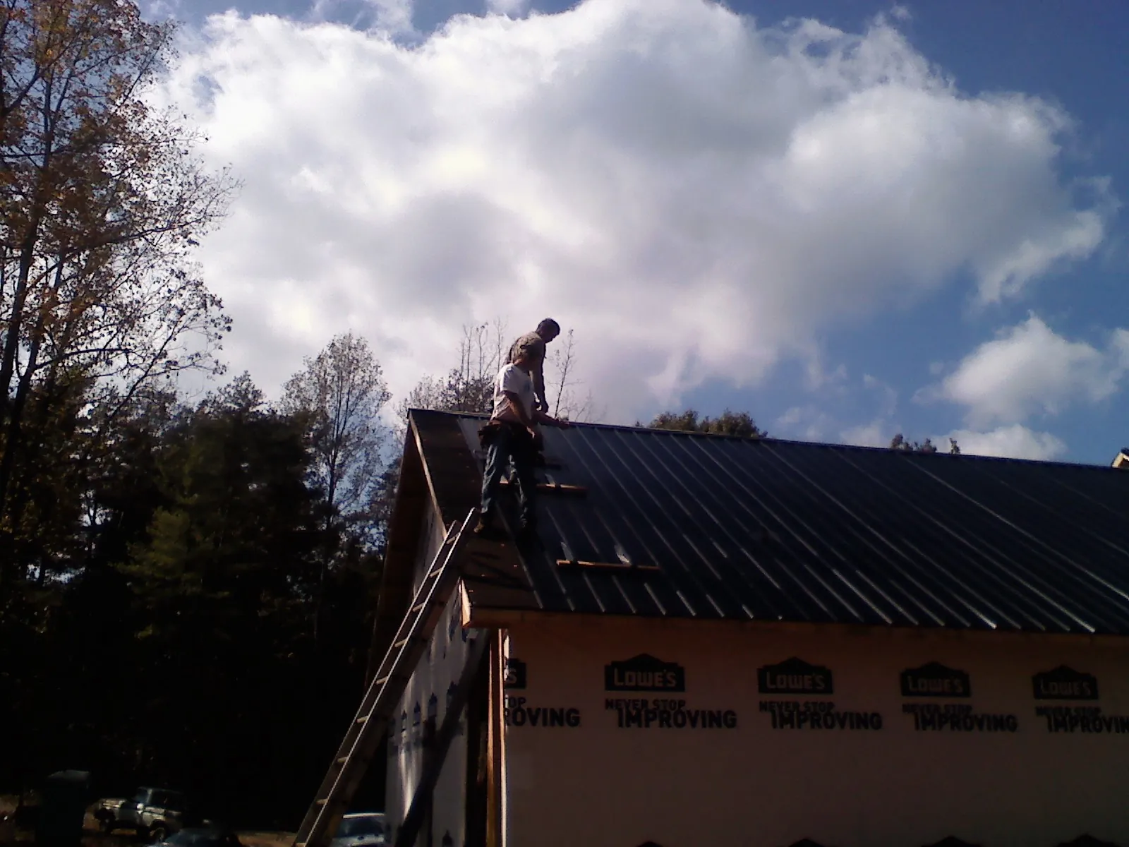 Roofer fastening dark metal panels high against a cloudy sky, from a Roof Inspection job in Deckerville